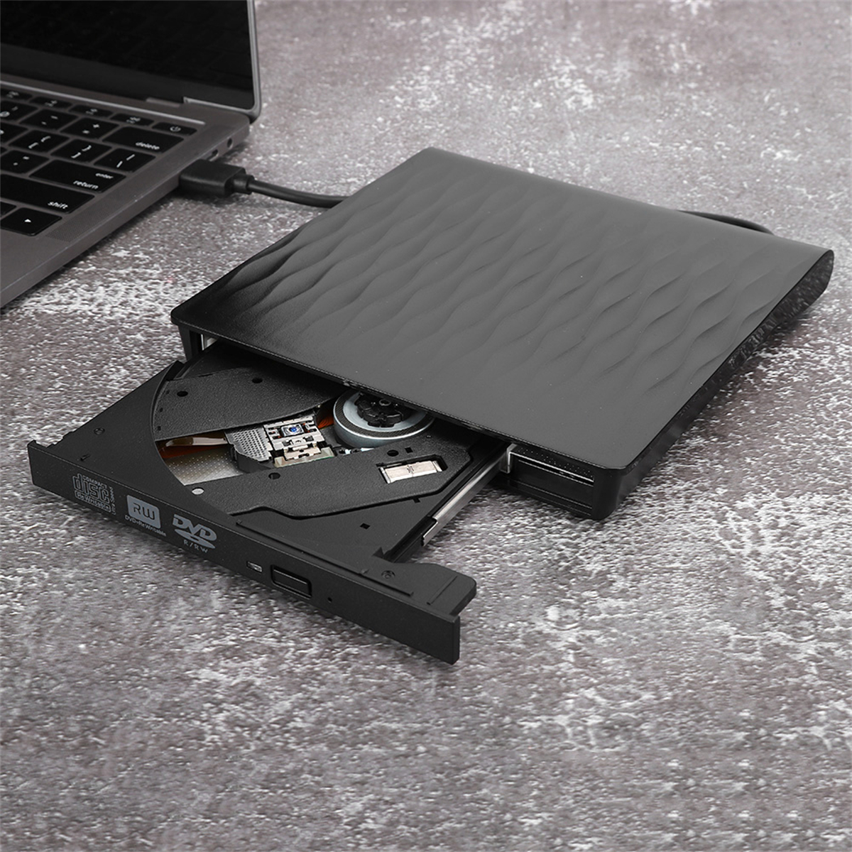 Schwarzes externes DVD-Laufwerk, geöffnet, um das Fach zu zeigen, an einen Laptop angeschlossen.