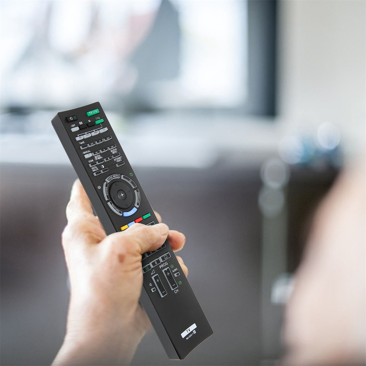 Hand hält eine schwarze Fernbedienung mit vielen Knöpfen, die sich auf einen Fernseher konzentriert.
