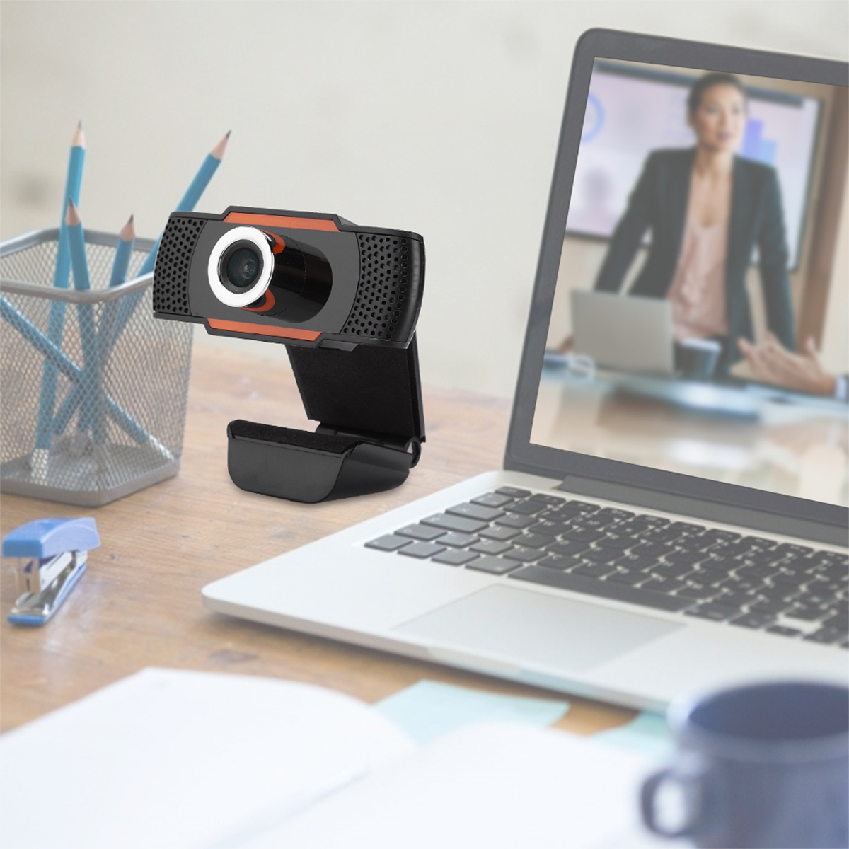 Webcam auf einem Schreibtisch, gerichtet auf Laptop mit Videoanruf. Stifthalter und Tacker auf dem Tisch.