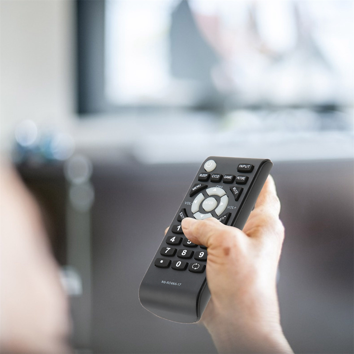 Hand hält schwarze Fernbedienung. Der Benutzer drückt eine Taste. Ein Fernseher im Hintergrund.