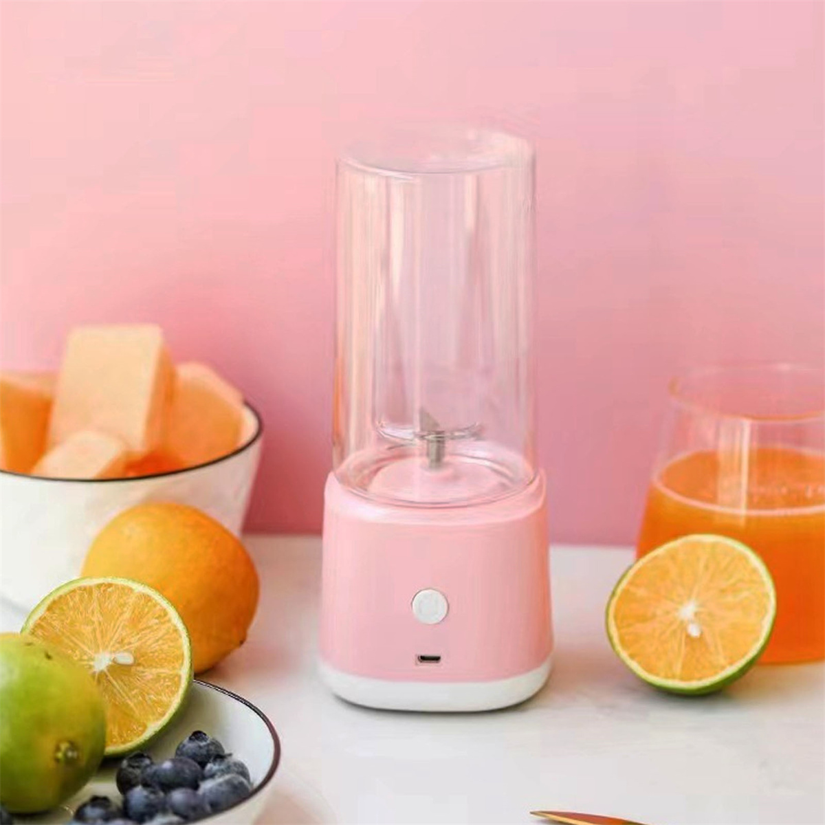 Ein rosa Mixer mit einem transparenten Behälter, neben Orangen und Blaubeeren auf rosa Hintergrund.