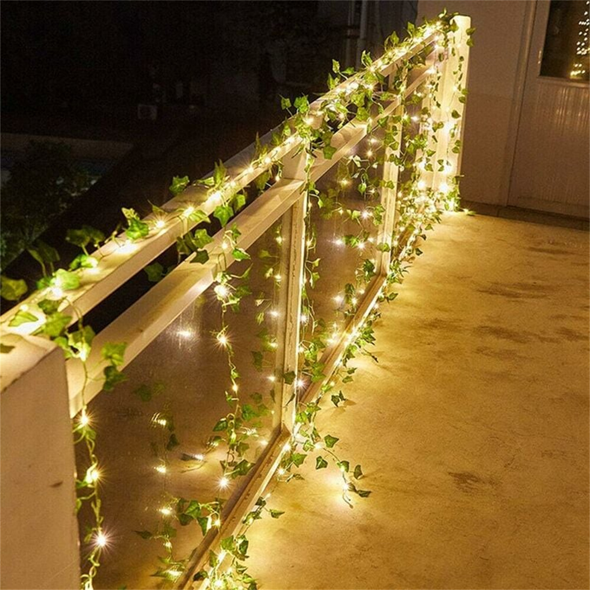 Ein weißes Geländer mit grünen Weinrebenlichtern, die eine nächtliche Atmosphäre schaffen.