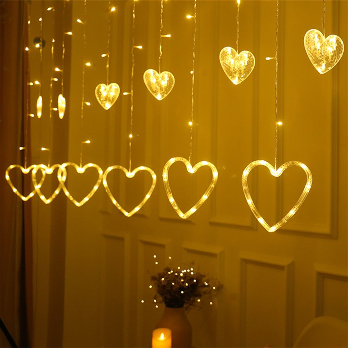 Lichter in Herzform hängen vor einer weißen Wand.