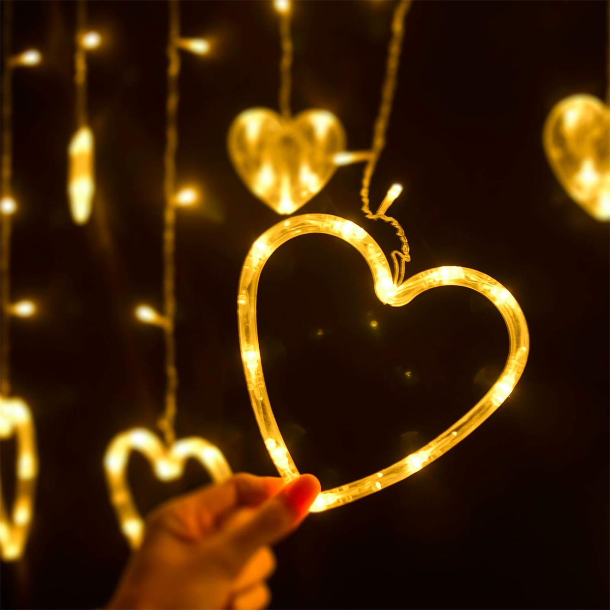 Hand hält ein beleuchtetes herzförmiges Licht. Andere Herzlichter sind im Hintergrund, alle gelb.