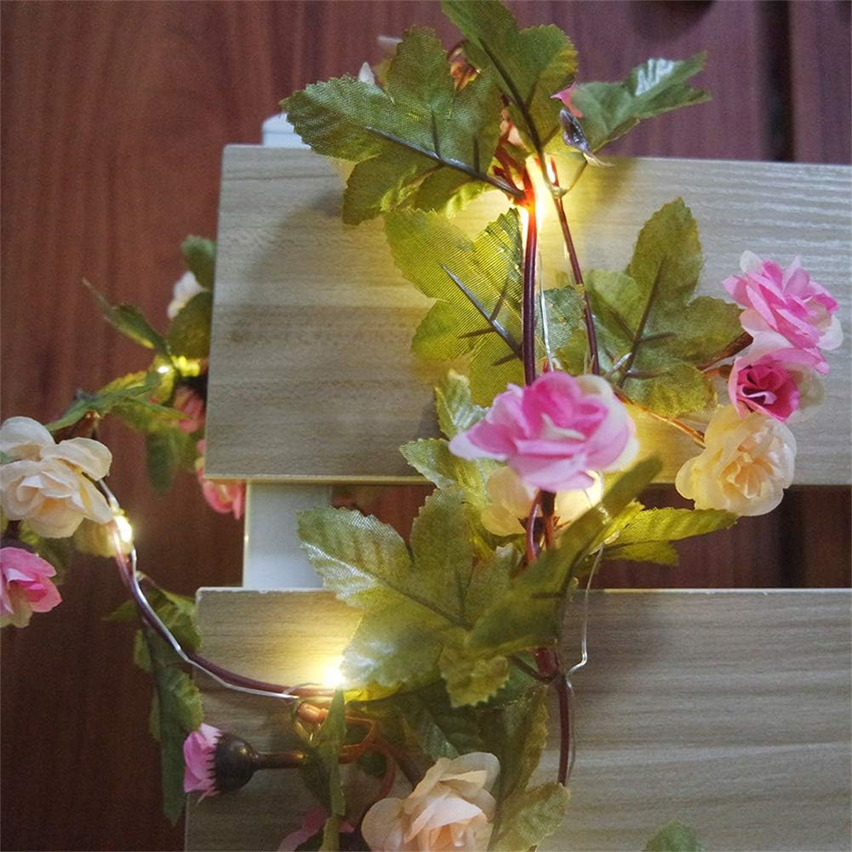 Lichterkette mit Blumen und Blättern. Grüne Blätter, rosa und weiße Blüten. Auf Holzbrettern platziert.