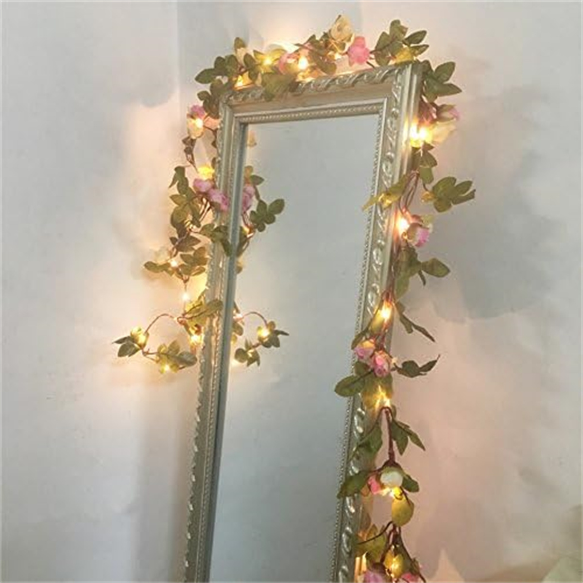 Ein silber eingerahmter Spiegel, verziert mit rosa und weißen Blumen und Lichterketten.