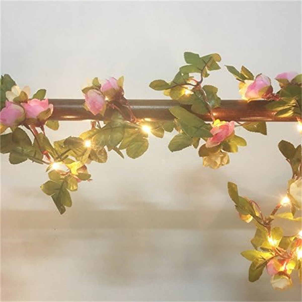 Eine Girlande aus rosa Rosen und grünen Blättern mit kleinen Lichtern, die entlang einer Holzstange gespannt sind.