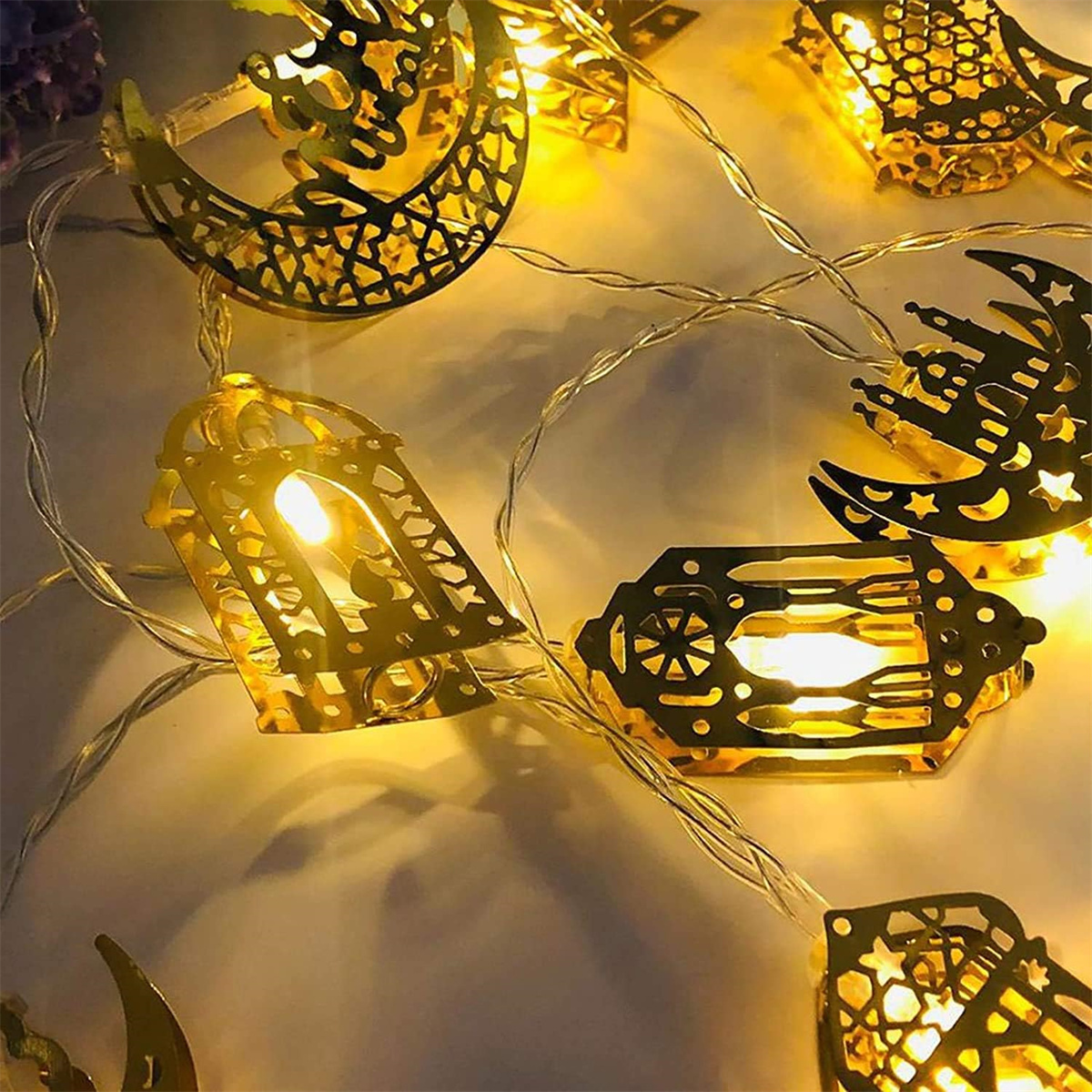 Lichterkette mit goldenen Laternen in verschiedenen Formen, beleuchtet auf weißer Oberfläche. Warmes Licht.