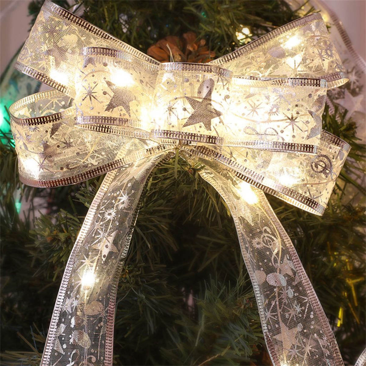 Eine dekorative Weihnachts-Schleife mit Lichtern, an einem grünen Baum hängend.