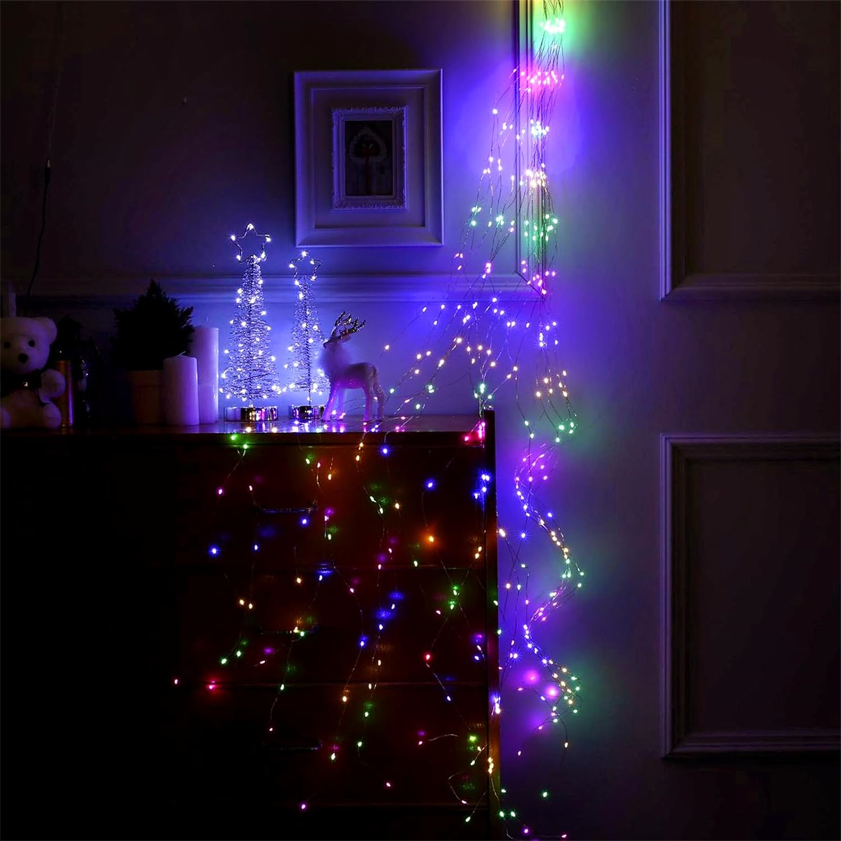 Ein dunkler Raum mit Lichterketten an einer Wand und einer Holzkommode. Ein gerahmtes Bild ist vorhanden.