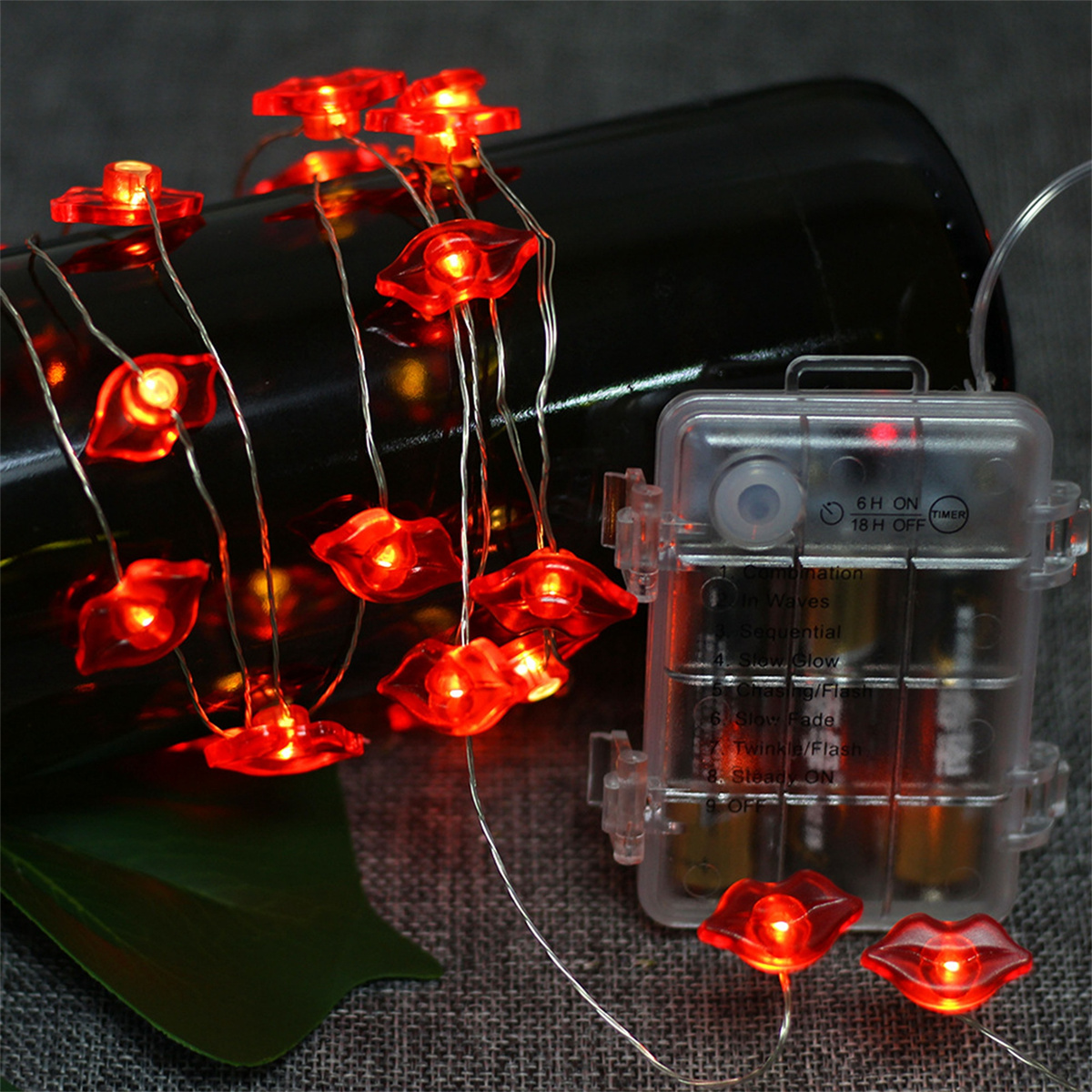 Eine Lichterkette mit roten Lippenlichtern auf einem Draht, mit einem transparenten Batteriepack auf dunklem Hintergrund.