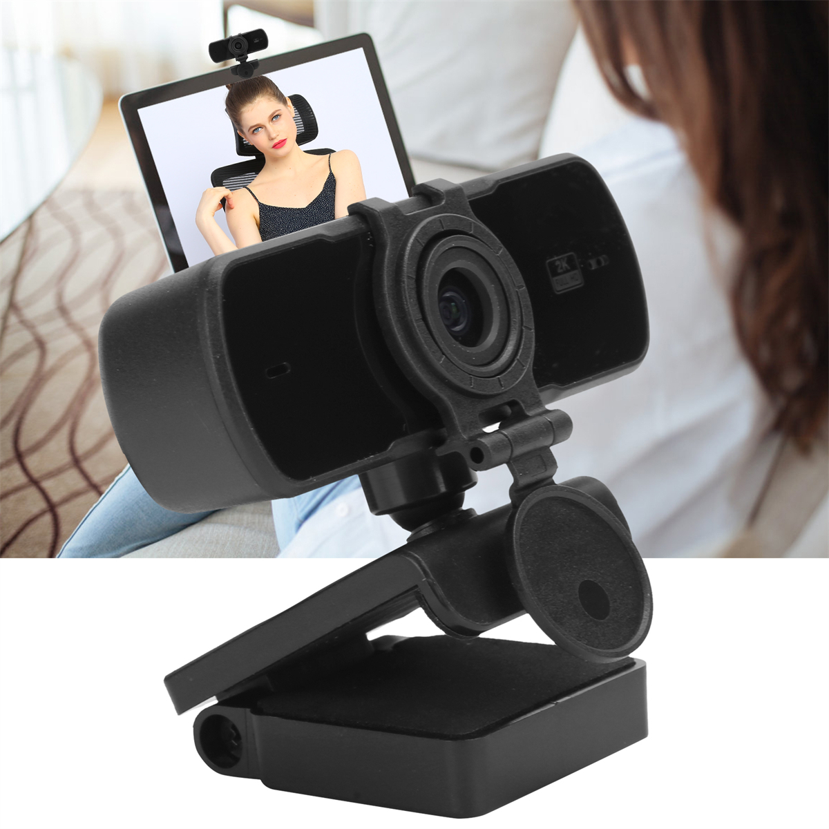 Eine schwarze Webcam ist an einem Laptop montiert, auf dem eine Frau zu sehen ist. Eine Person ist im Hintergrund unscharf.