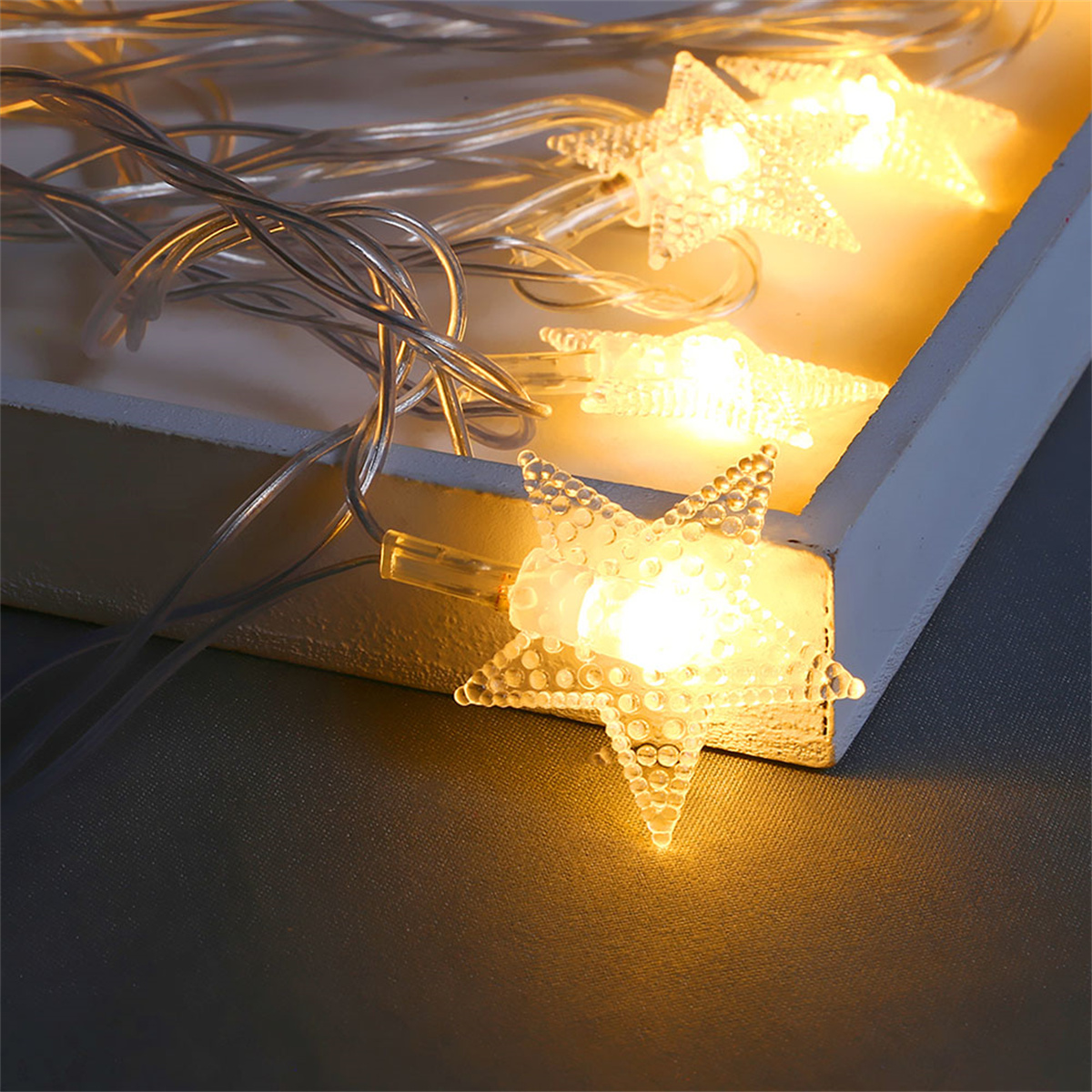 Nahaufnahme von sternförmigen Lichtern auf einem weißen Holztablett. Die Lichter leuchten warm.