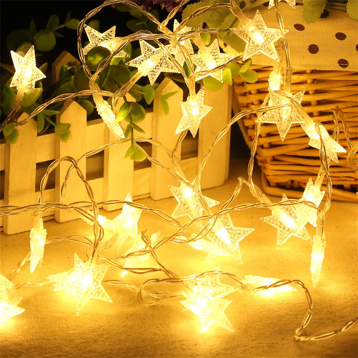 Sternförmige Lichterketten, warm leuchtend, vor einem weißen Zaun angeordnet.