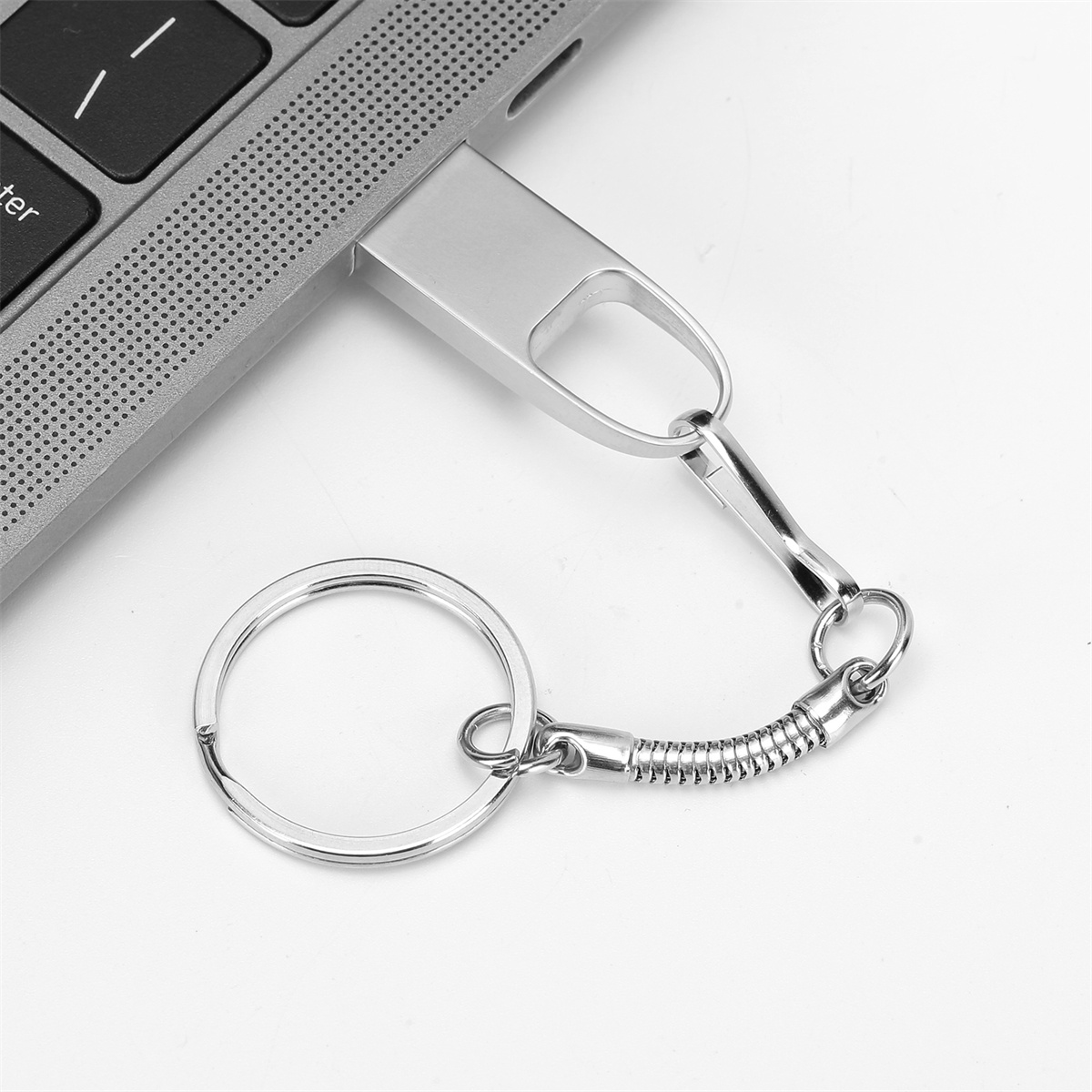 Silberner USB-Stick mit Schlüsselanhänger, an einen Laptop angeschlossen. Weißer Hintergrund.