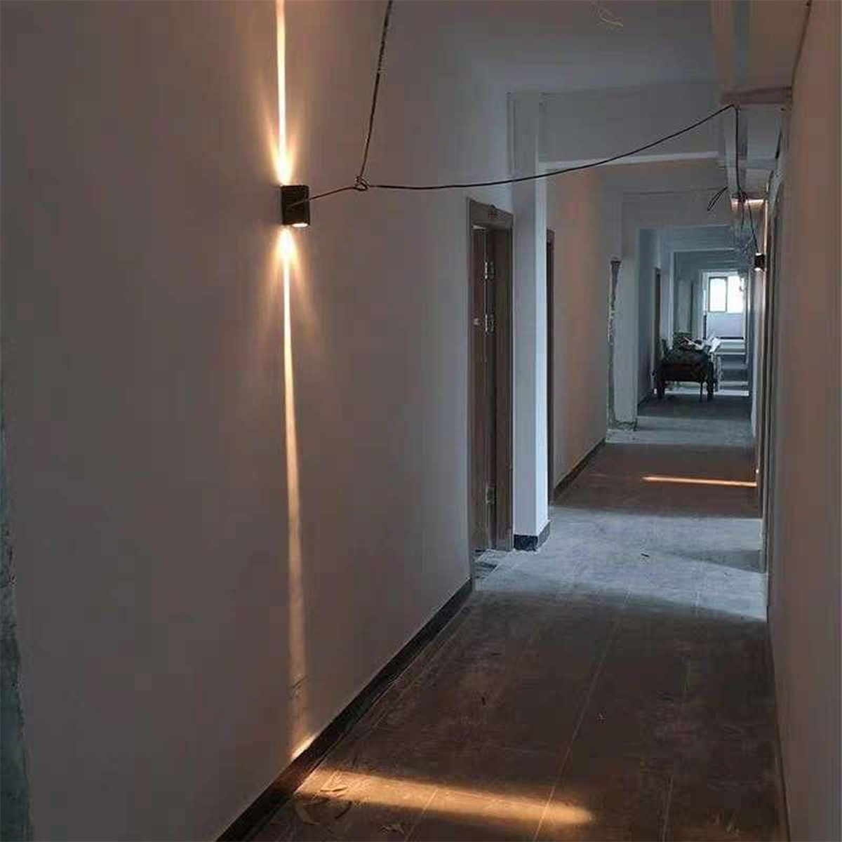 Flur mit Lichtvorrichtungen. Zwei Lichter an der Wand, die nach unten scheinen, wodurch ein heller Pfad entsteht.