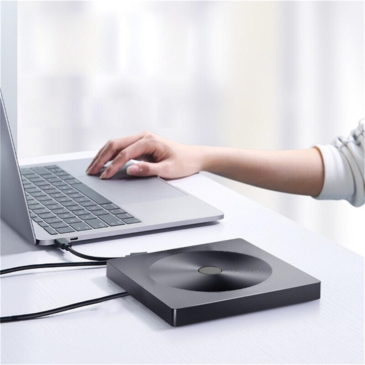 Person benutzt Laptop, mit schwarzem, rundem Gerät daneben, auf weißer Oberfläche.