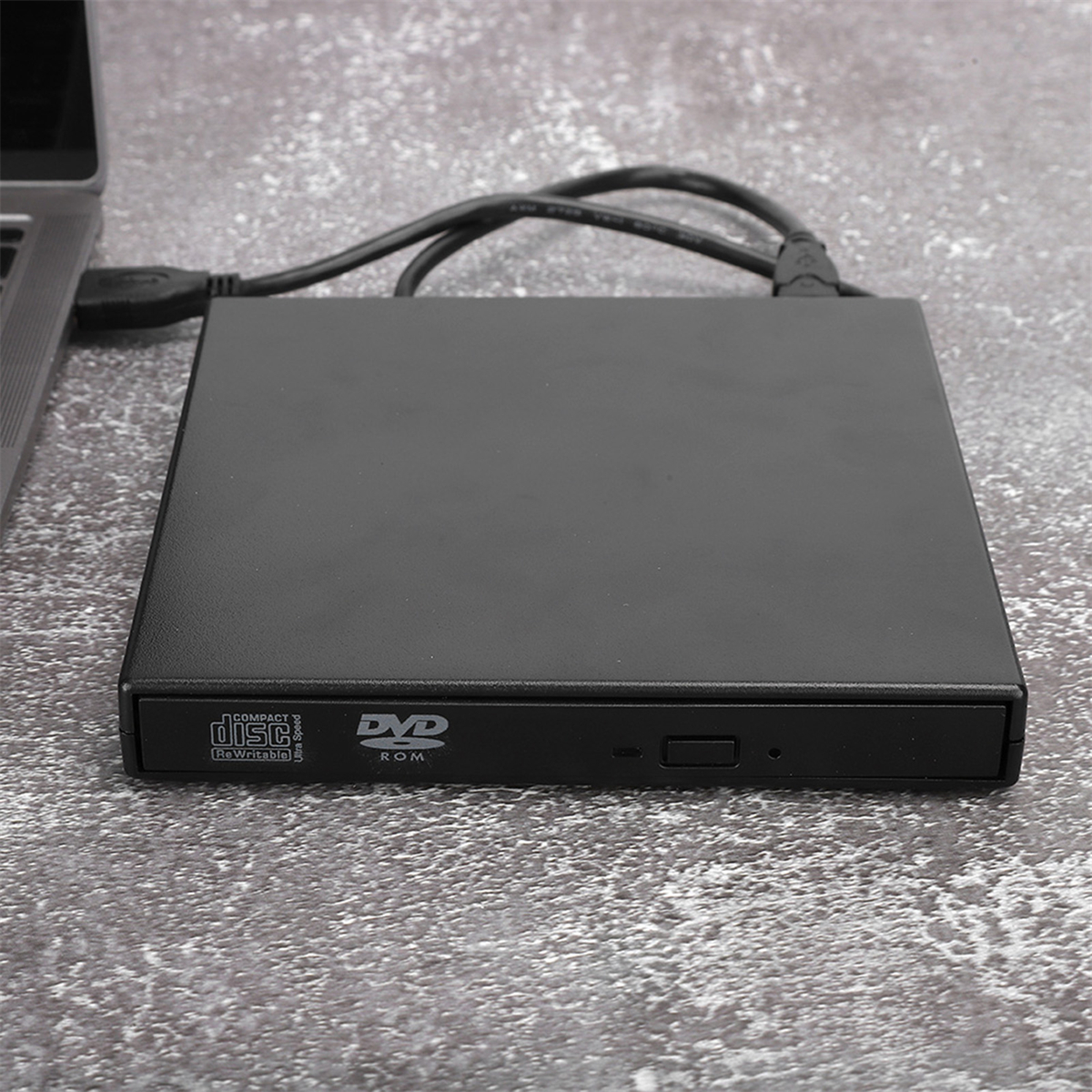 Schwarzes DVD/CD-Laufwerk, an einen Laptop angeschlossen, auf grauer, strukturierter Oberfläche.