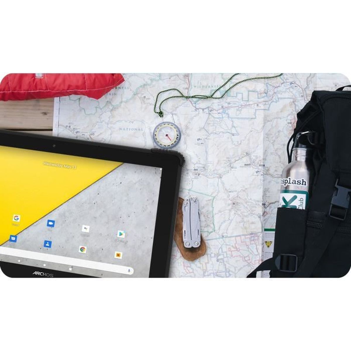 Tablet, kompas, butelka wody i multi-tool na mapie. Plecak i czerwona kurtka w pobliżu.