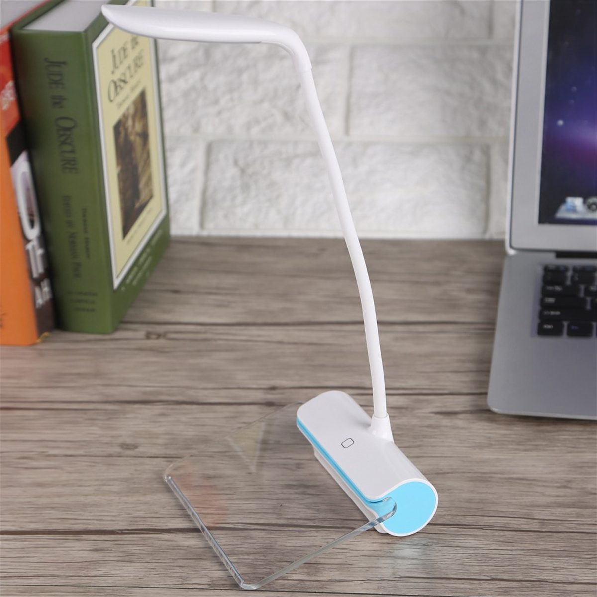 Weiße Schreibtischlampe mit flexiblem Hals. Bücher und Laptop im Hintergrund, auf einem Holztisch.
