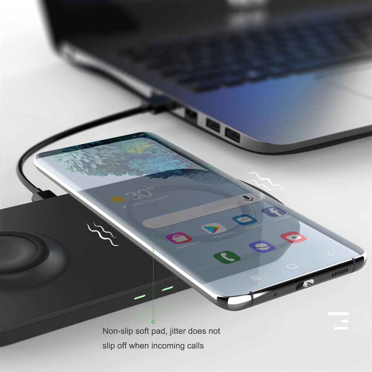 Ein Telefon, das drahtlos auf einem schwarzen Pad neben einem Laptop aufgeladen wird. Telefon zeigt App-Symbole.