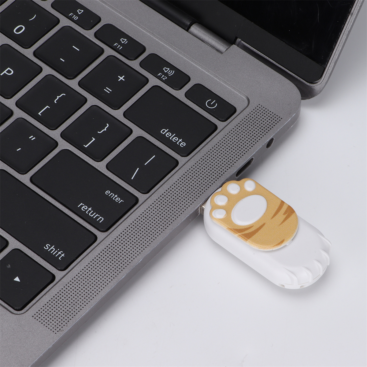Laptop-Tastatur mit einem pfotenförmigen USB-Stick. Der Stick ist weiß mit einer Katzenpfote.