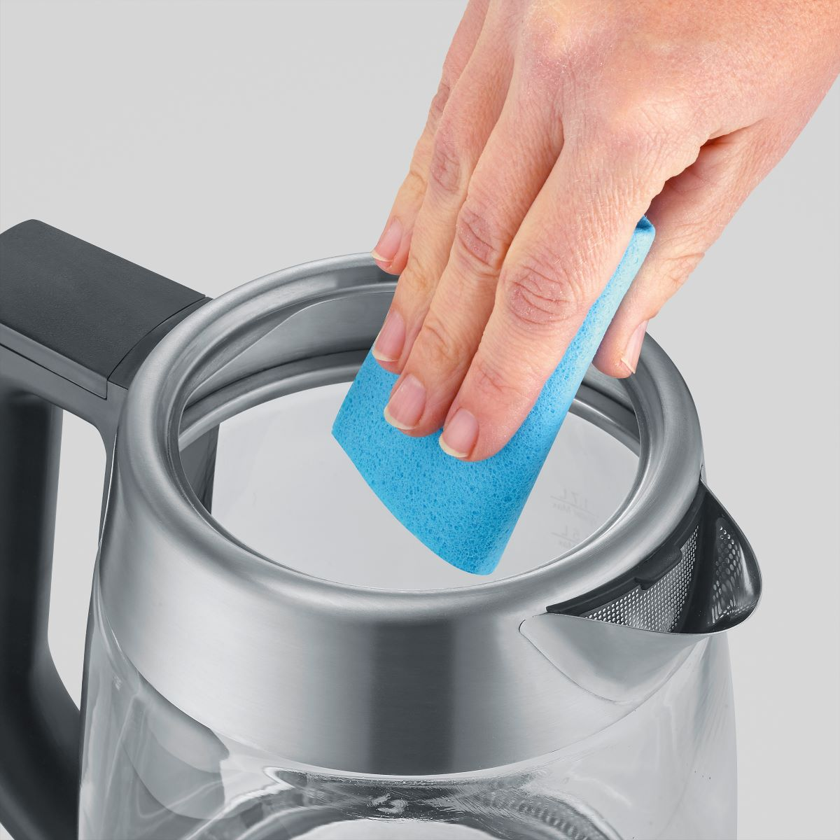 Close-up van een hand die de binnenkant van een waterkoker schoonmaakt met een blauwe spons.