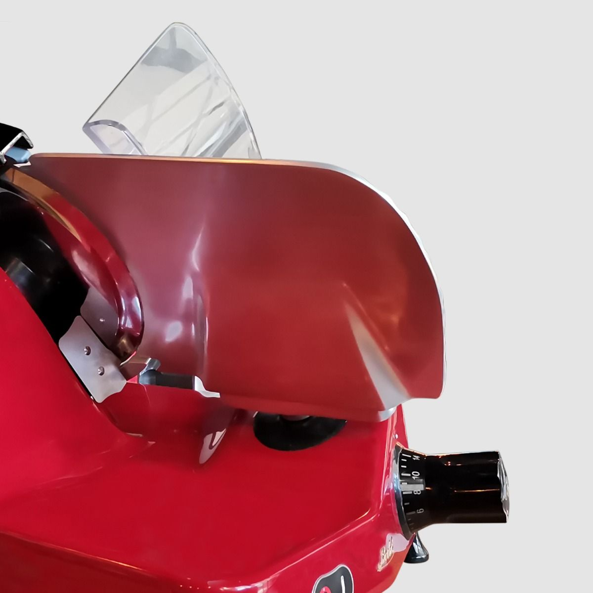 Primo piano di un'affettatrice rossa con protezione trasparente e manopola nera.