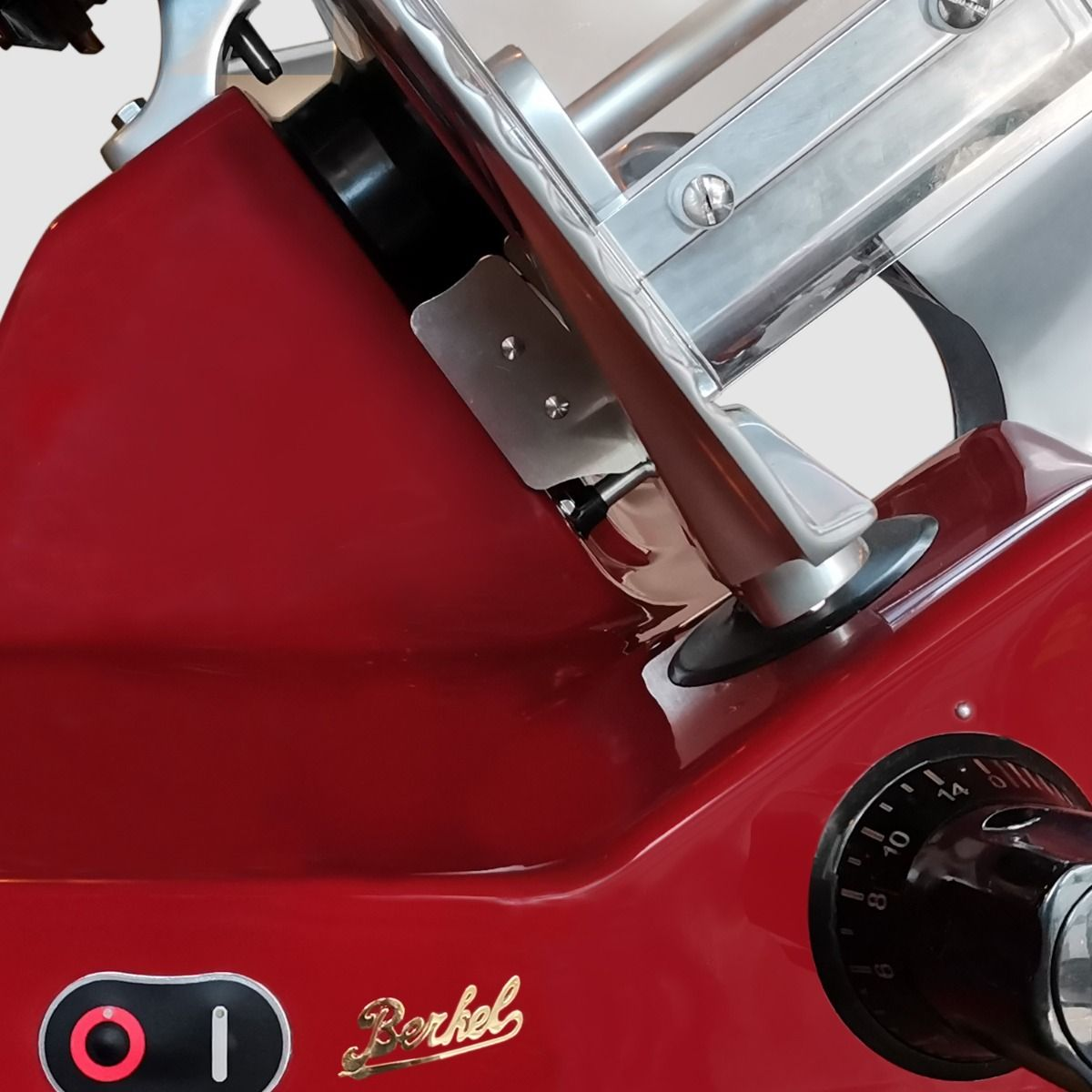 Primo piano di un'affettatrice Berkell rossa con lama in acciaio inox e manico nero, su superficie bianca.
