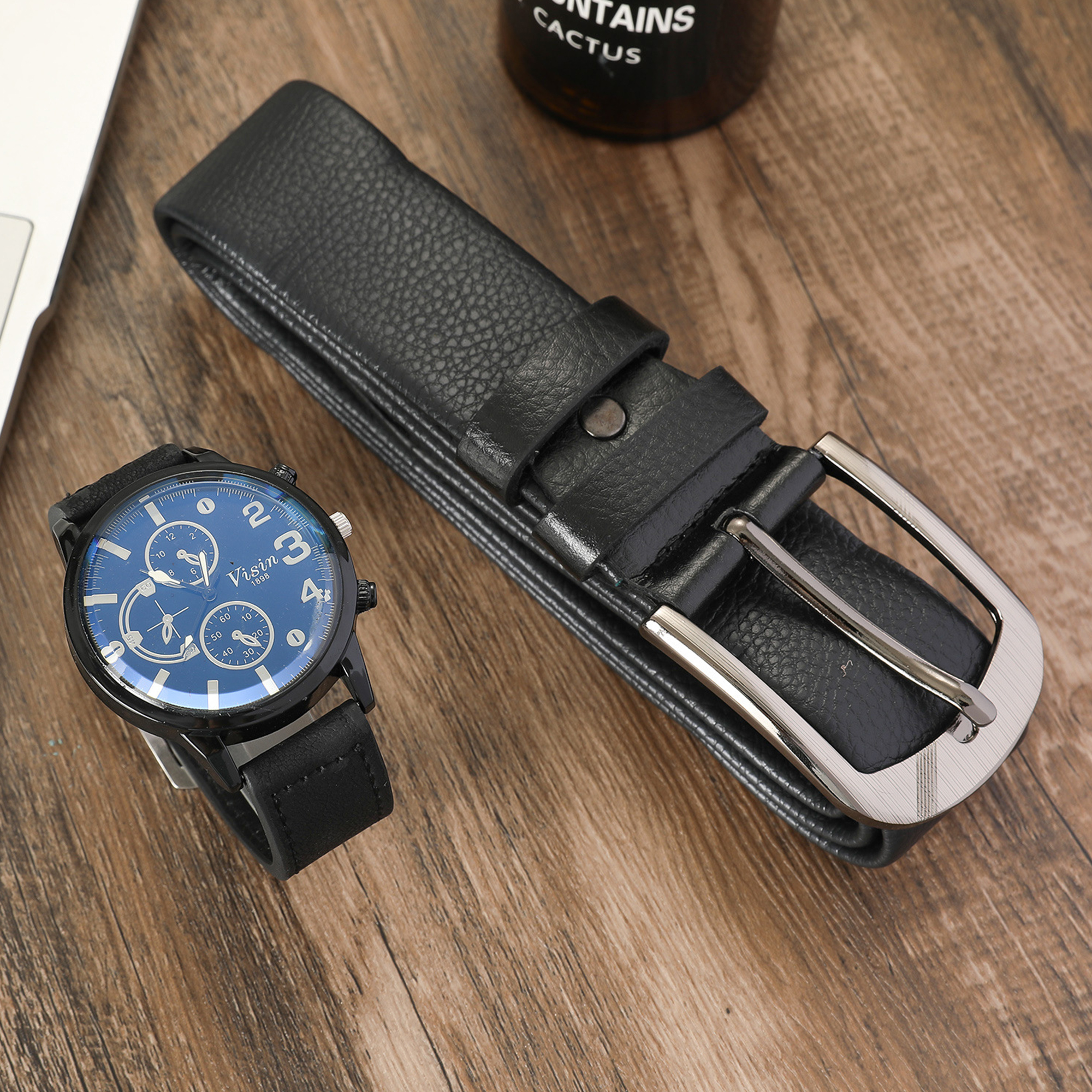 Schwarzer Ledergürtel, Armbanduhr mit blauem Zifferblatt und eine Kaktusflasche auf Holz.