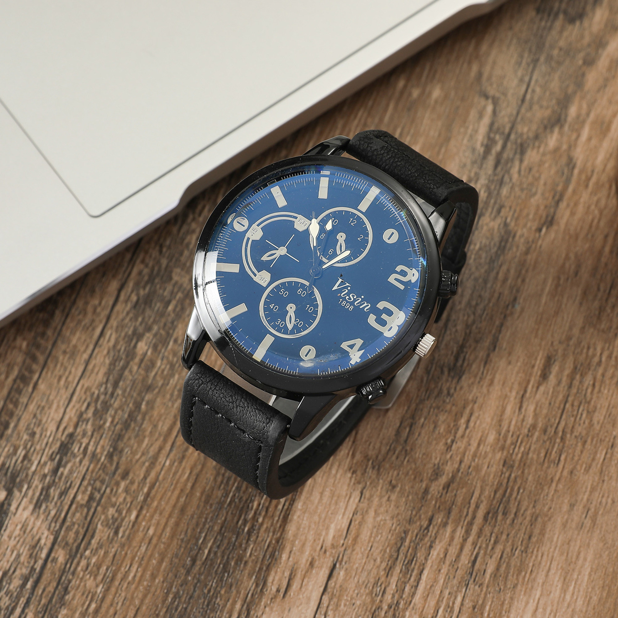 Eine schwarze Armbanduhr auf Holz, mit blauem Zifferblatt und schwarzem Lederarmband.