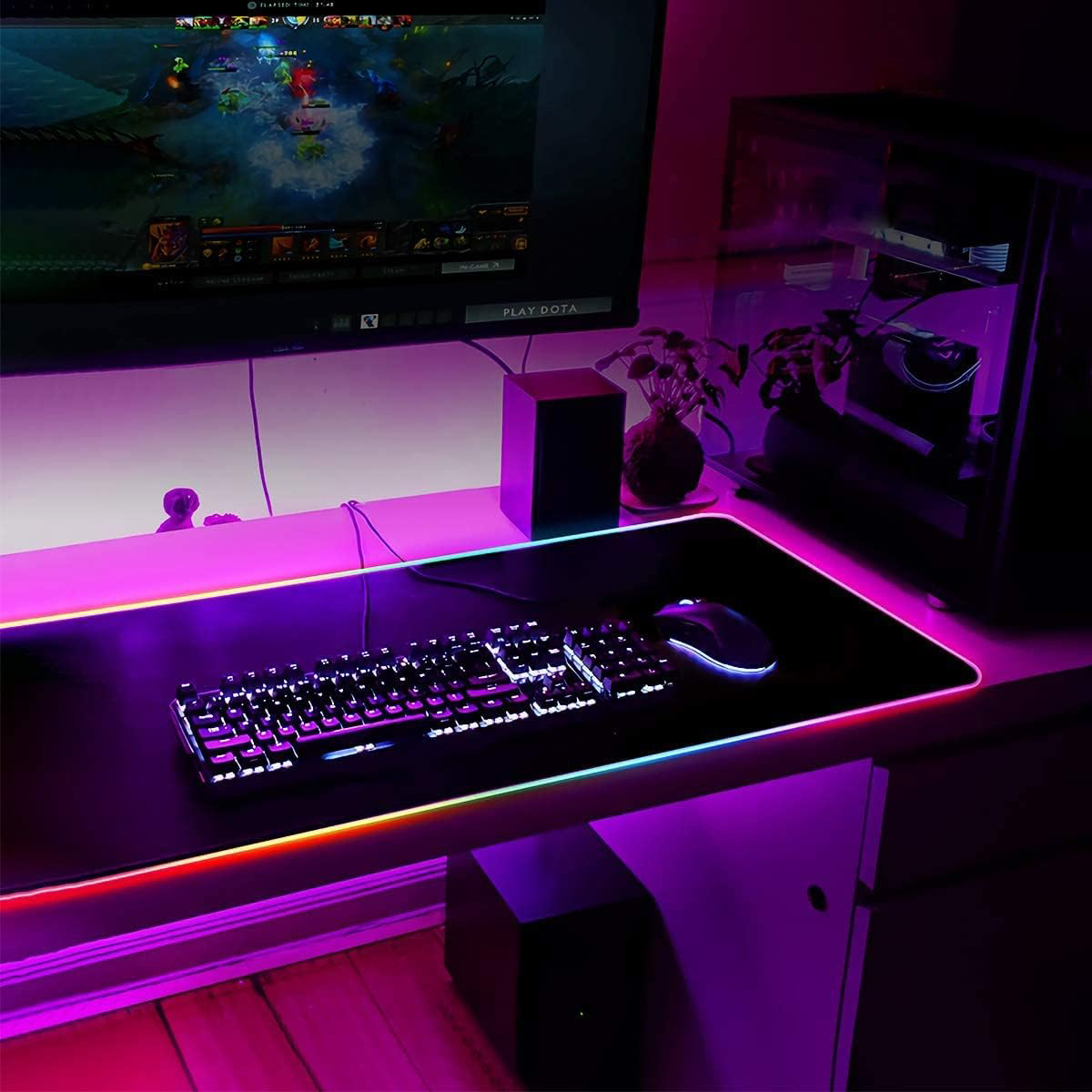 Gaming-Setup mit RGB-Beleuchtung, einschließlich Tastatur, Maus und großer Schreibtischunterlage. Monitor zeigt Spiel.