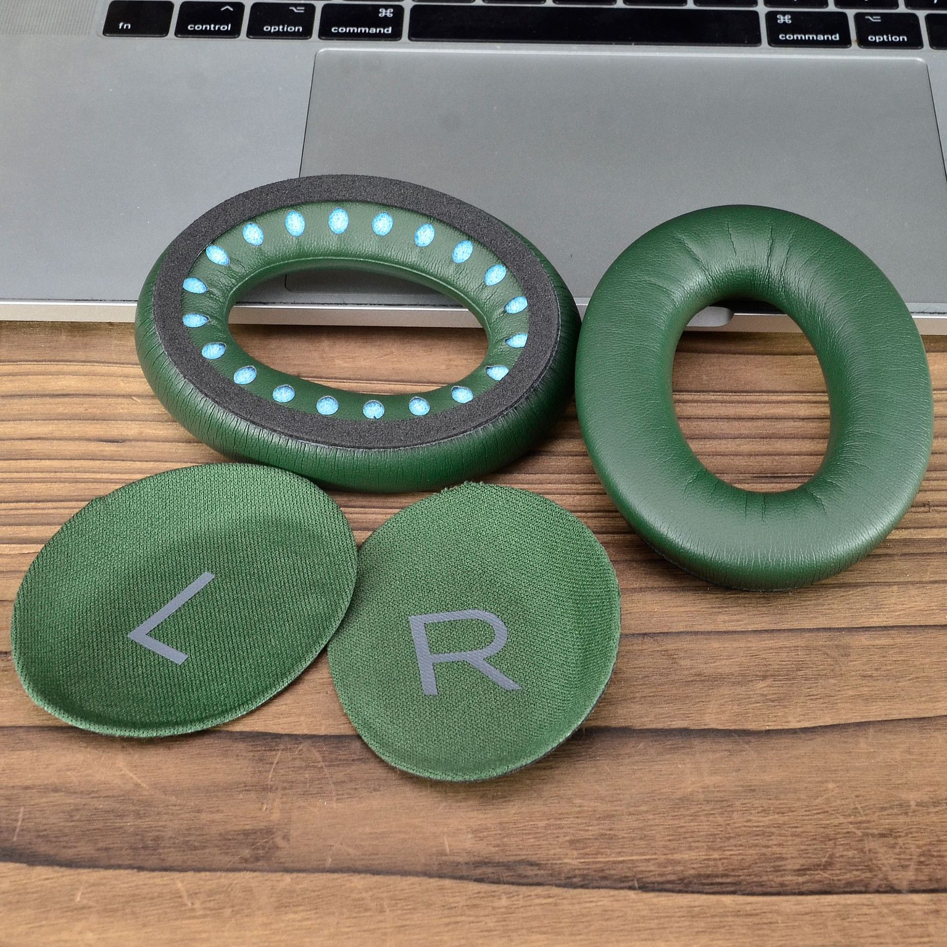 Poduszki i wkładki do słuchawek w kolorze zielonym, z otwartym laptopem w tle na drewnianej powierzchni.