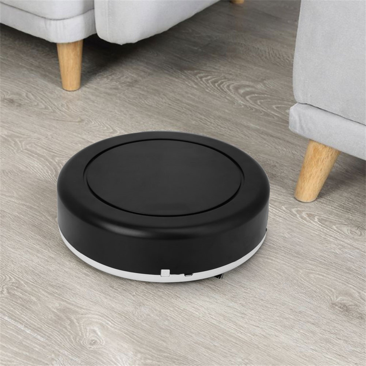 Schwarzer Roboter-Staubsauger auf Holzboden. Zwei graue Sofas im Hintergrund.