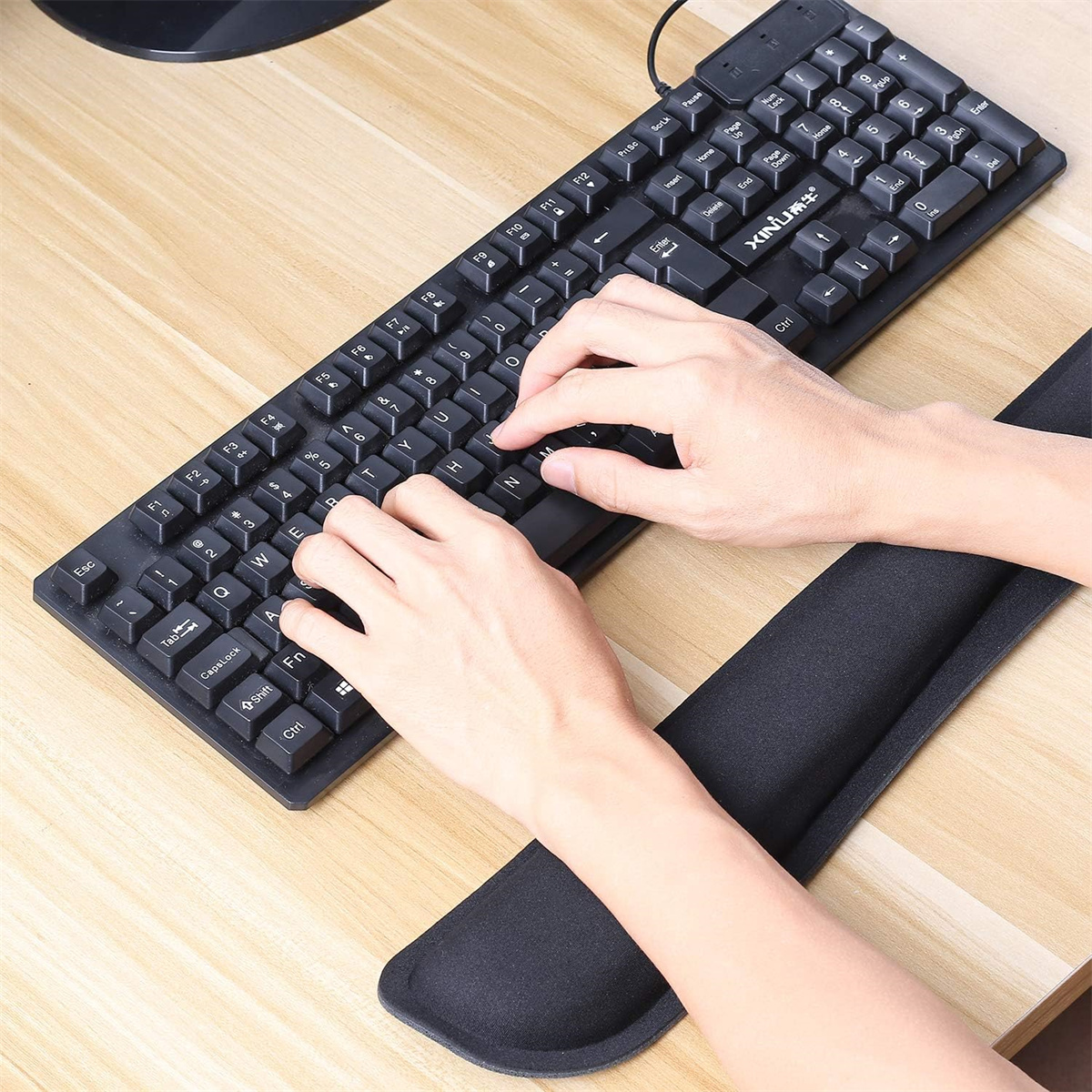 Hände auf Tastatur, mit schwarzer Tastatur und Handgelenkauflage auf einem Holzschreibtisch.