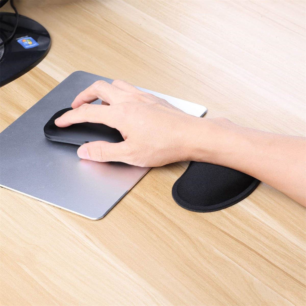 Hand mit schwarzer Maus und schwarzer Handgelenkstütze auf silbernem Mauspads und Holztisch.