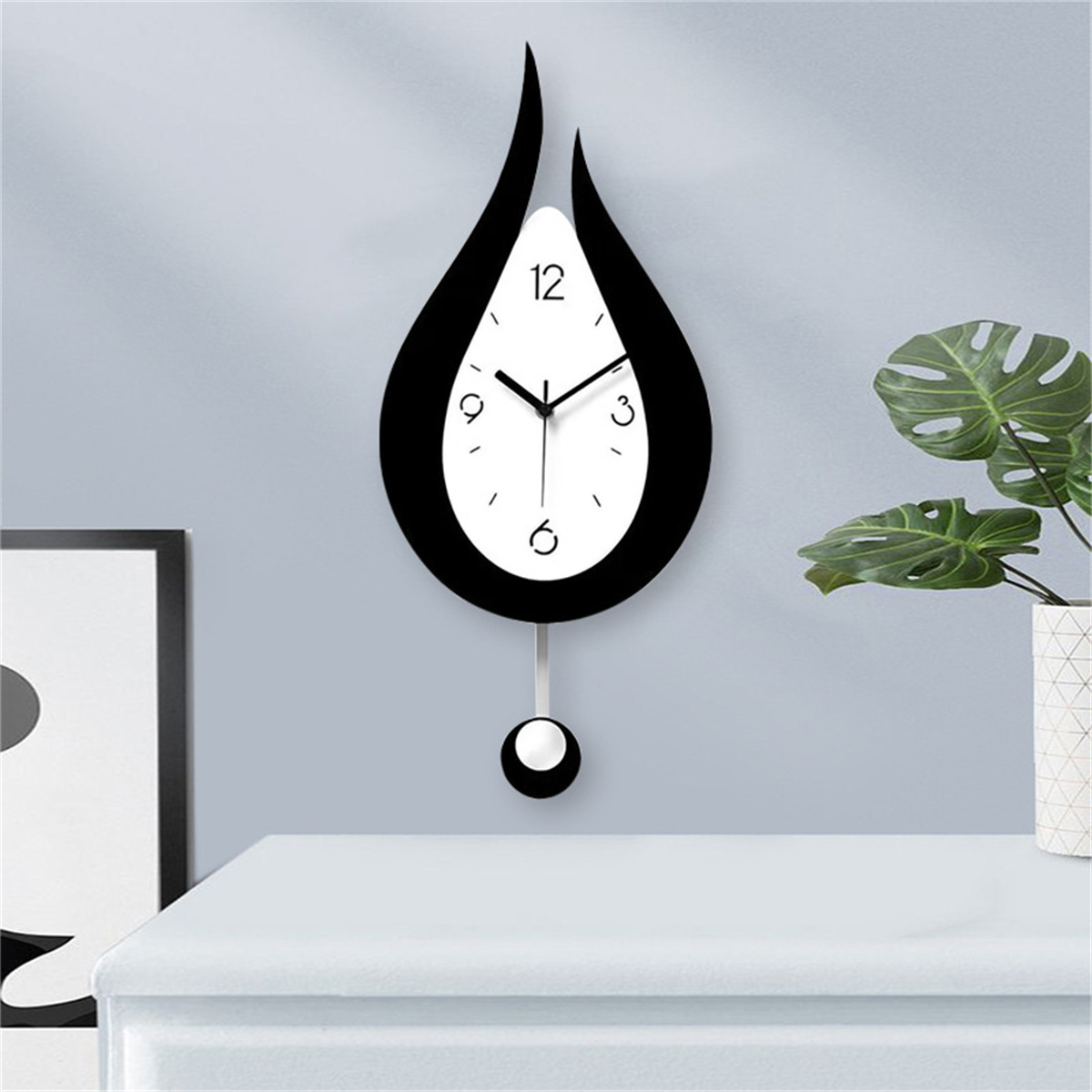 Eine schwarz-weiße tropfenförmige Uhr mit Pendel, an einer grauen Wand montiert.