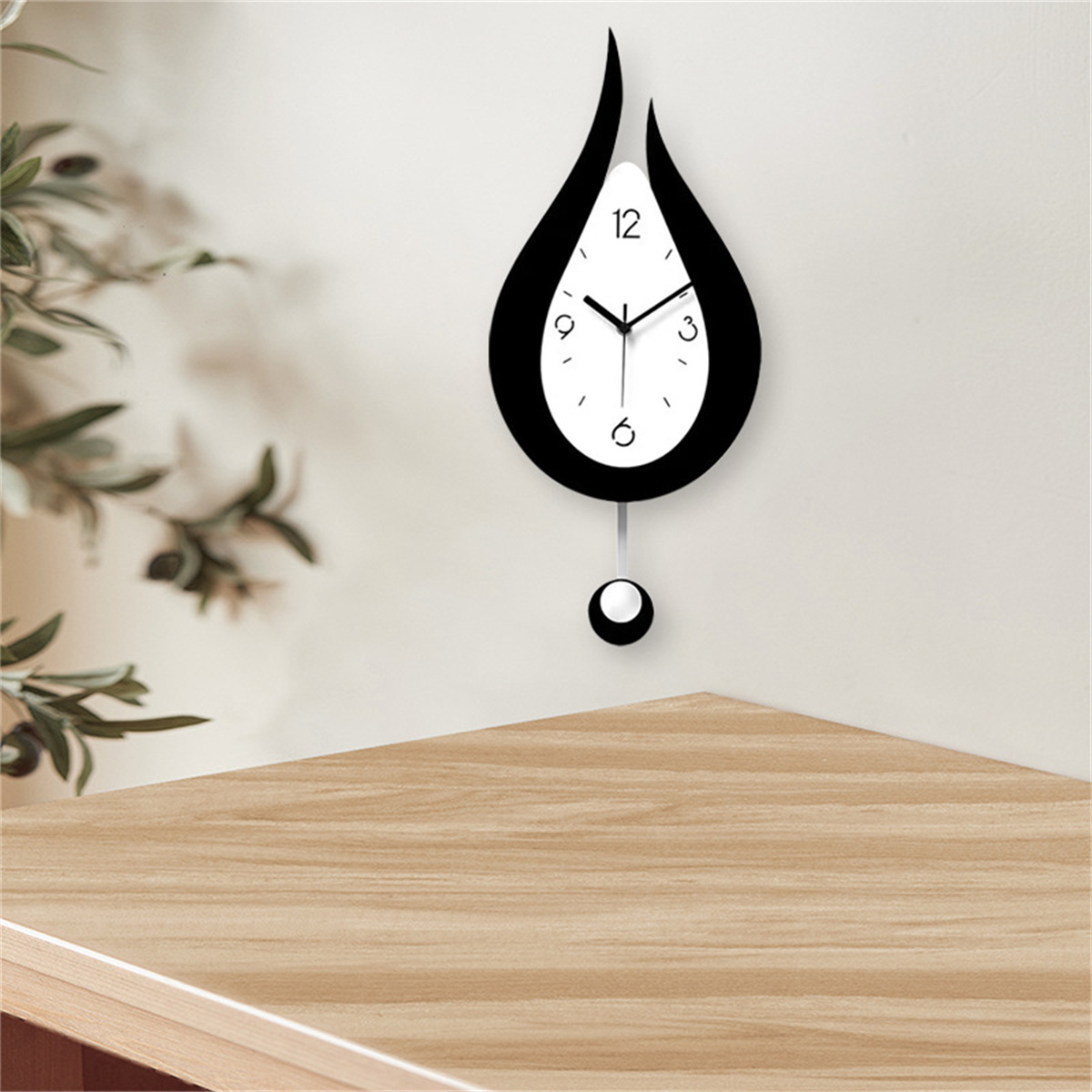Schwarz-weiße tropfenförmige Wanduhr. Ecke eines Holztisches. Weiße Wand.