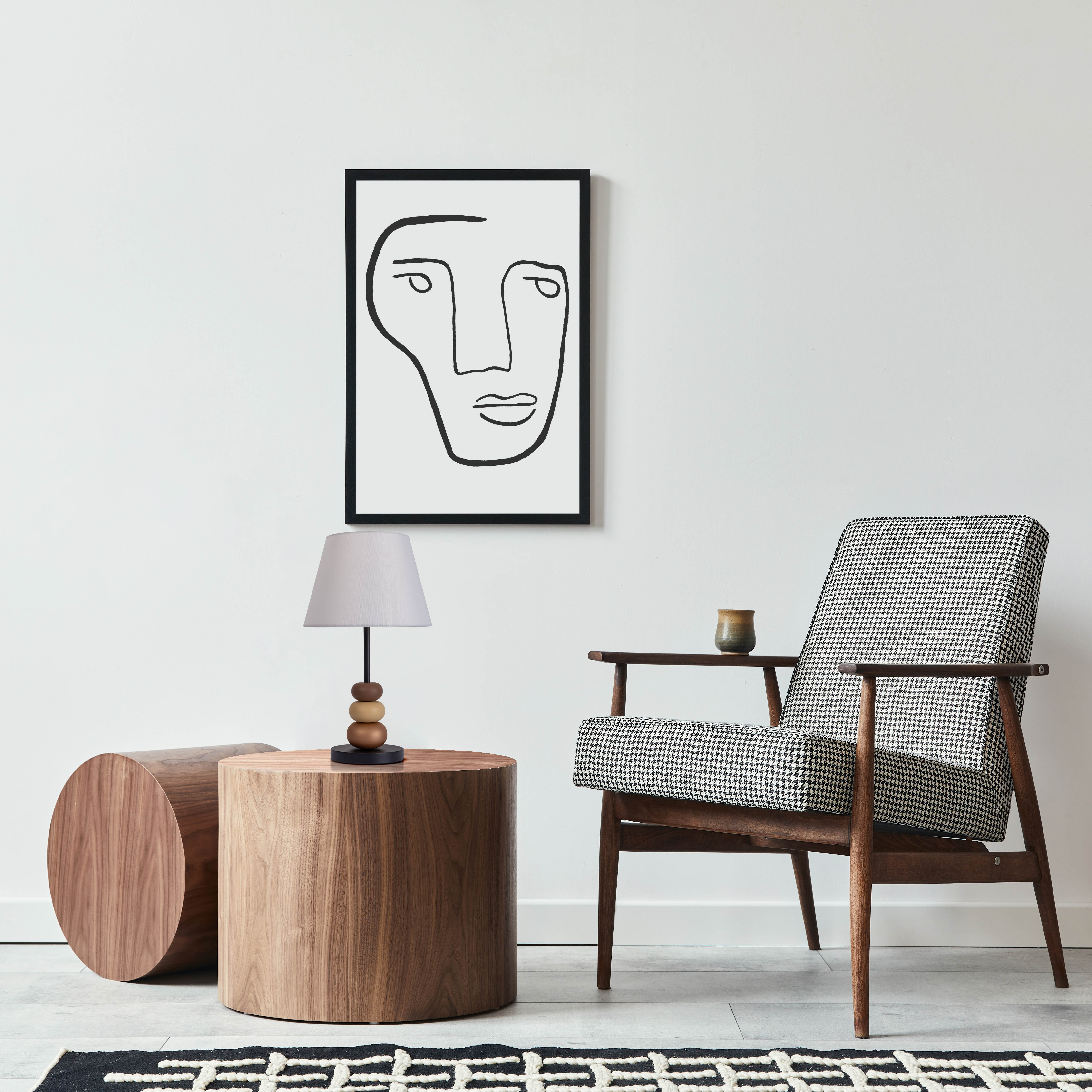 Raumszene mit Stuhl, Tisch, Lampe und Kunstwerk. Ein Teppich liegt auf dem Boden.