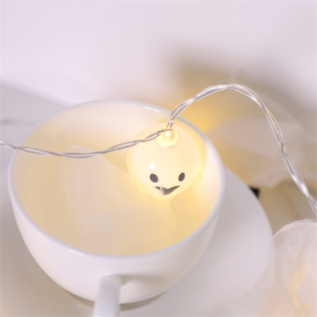 Eine lächelnde, leuchtende Glühbirne in einer Teetasse mit Untertasse. Das Licht strahlt warm.