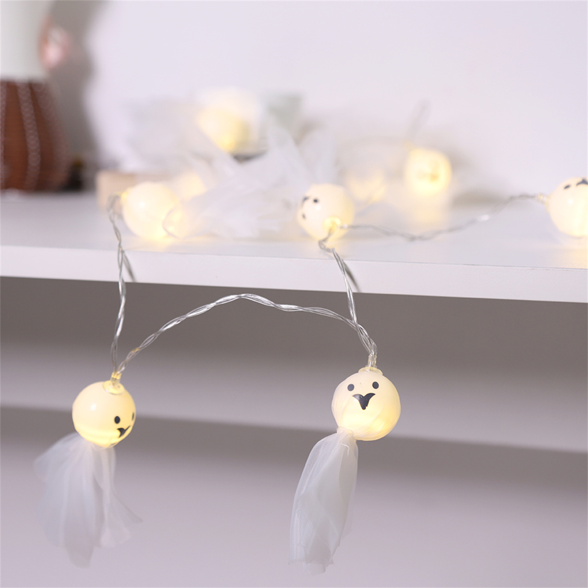 Lichterketten in Geisterform. Die Lichter sind weiß mit weißem Tüllrock. Sie liegen auf einem Regal.