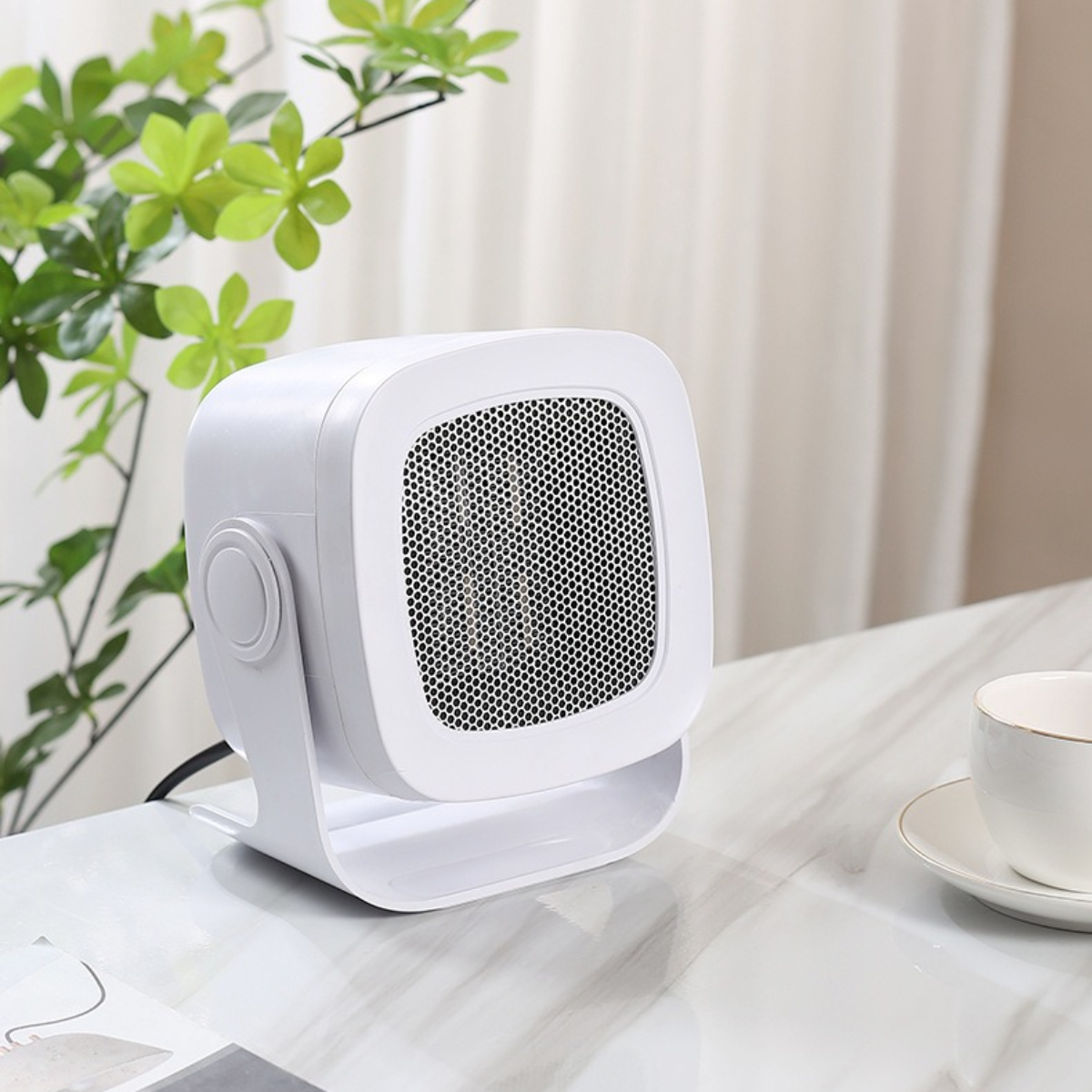 Weißer Elektroheizer auf einem Tisch mit einer Tasse und einer grünen Pflanze.