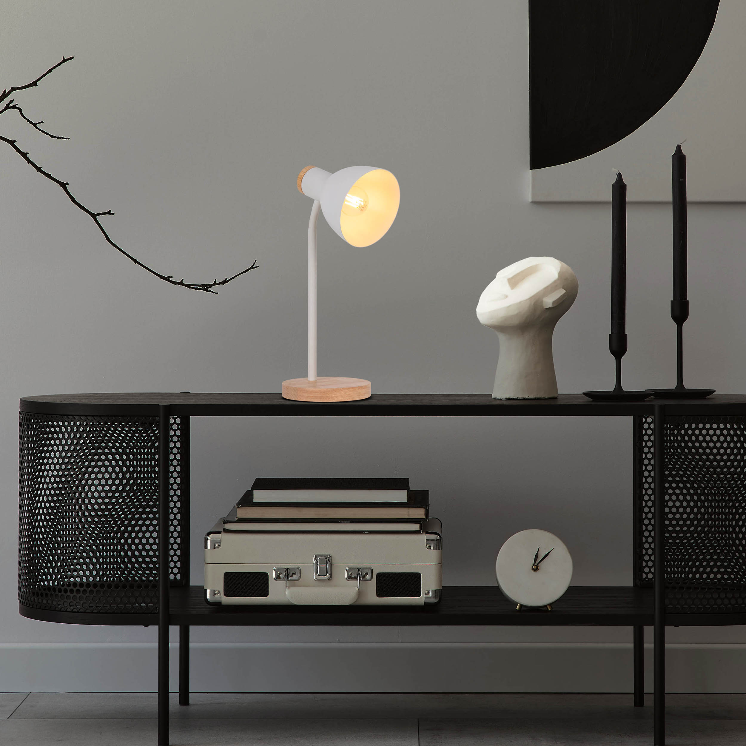 Schreibtischlampe auf Holzsockel. Schwarzes Regal mit Büchern, Kisten, Kopfskulptur und Kerzen.