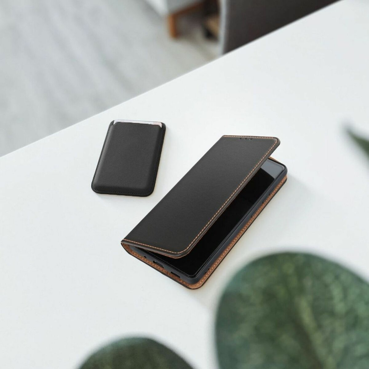 Una custodia per telefono nera con un telefono all'interno, accanto a un portacarte più piccolo su una superficie bianca.