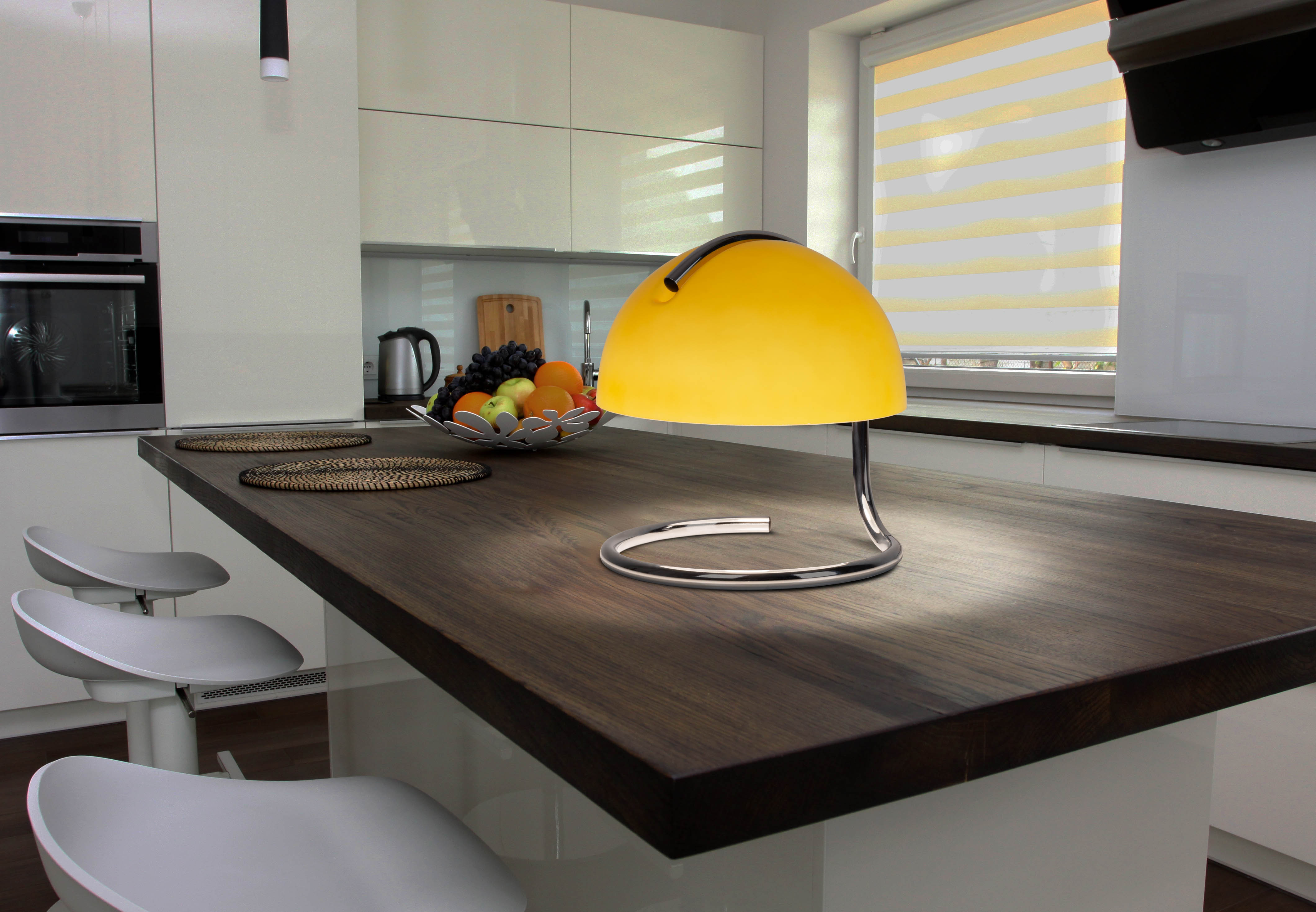 Eine gelbe Lampe auf einer dunklen Holz-Arbeitsplatte in einer modernen Küche mit weißen Schränken.
