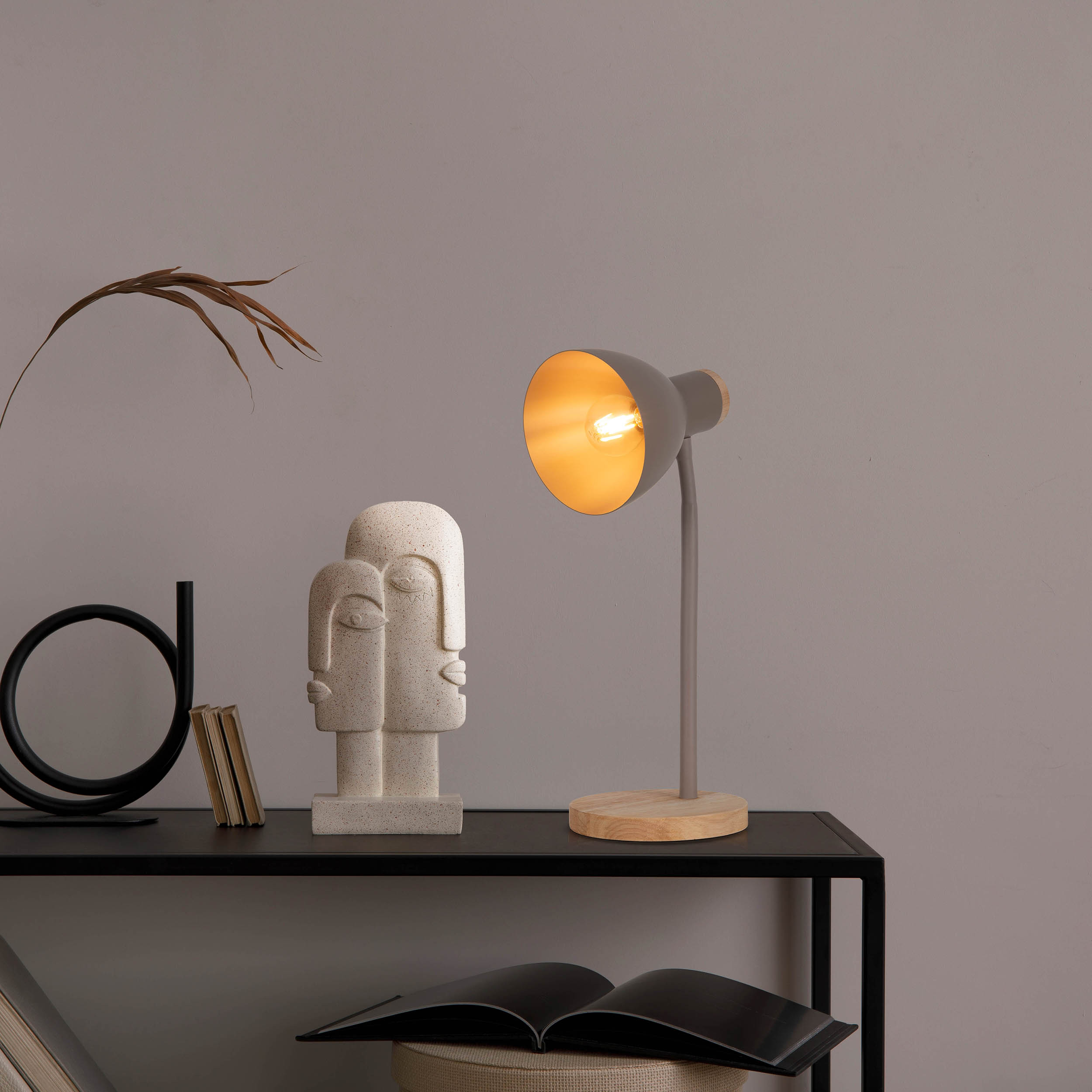 Schreibtischlampe mit grauem Schirm, Holzsockel und Statue auf schwarzem Tisch.