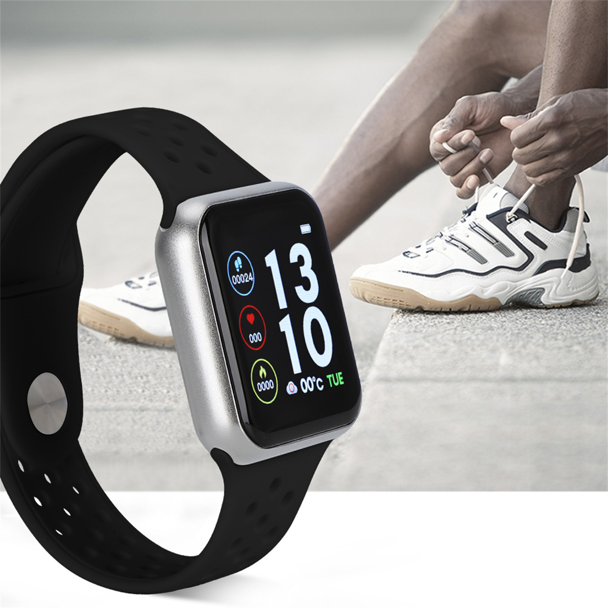 Eine schwarze Smartwatch mit schwarzem Armband. Eine Person bindet im verschwommenen Hintergrund ihre Schnürsenkel.