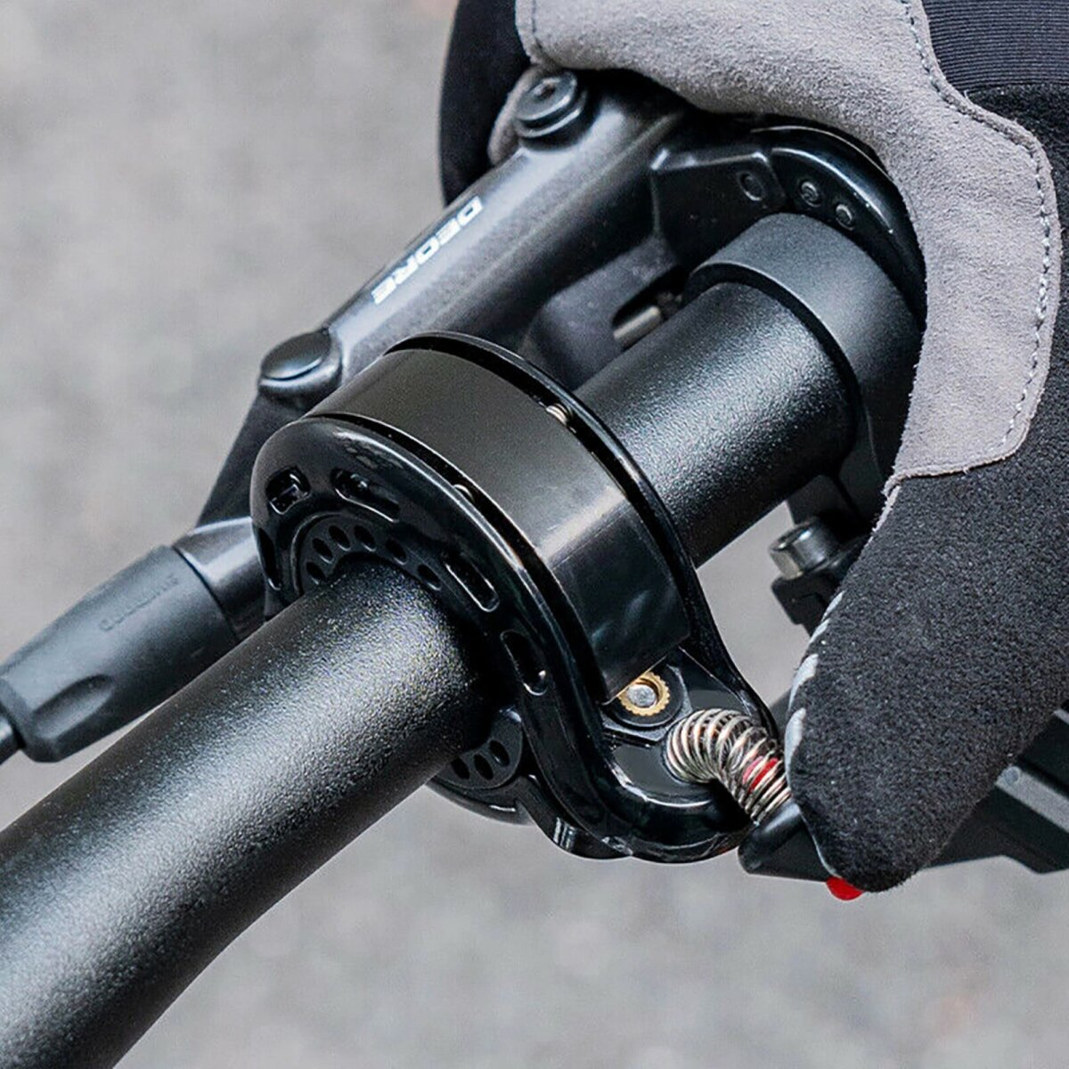 Ein schwarzer Fahrradlenker mit einem schwarzen Gerät befestigt. Eine behandschuhte Hand hält es.