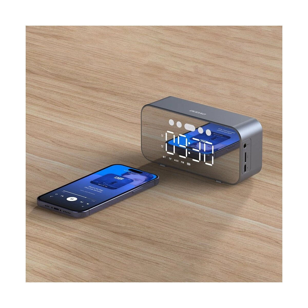 Ein spiegelbeschichteter Lautsprecher und ein Smartphone auf Holz. Der Lautsprecher zeigt die Zeit.