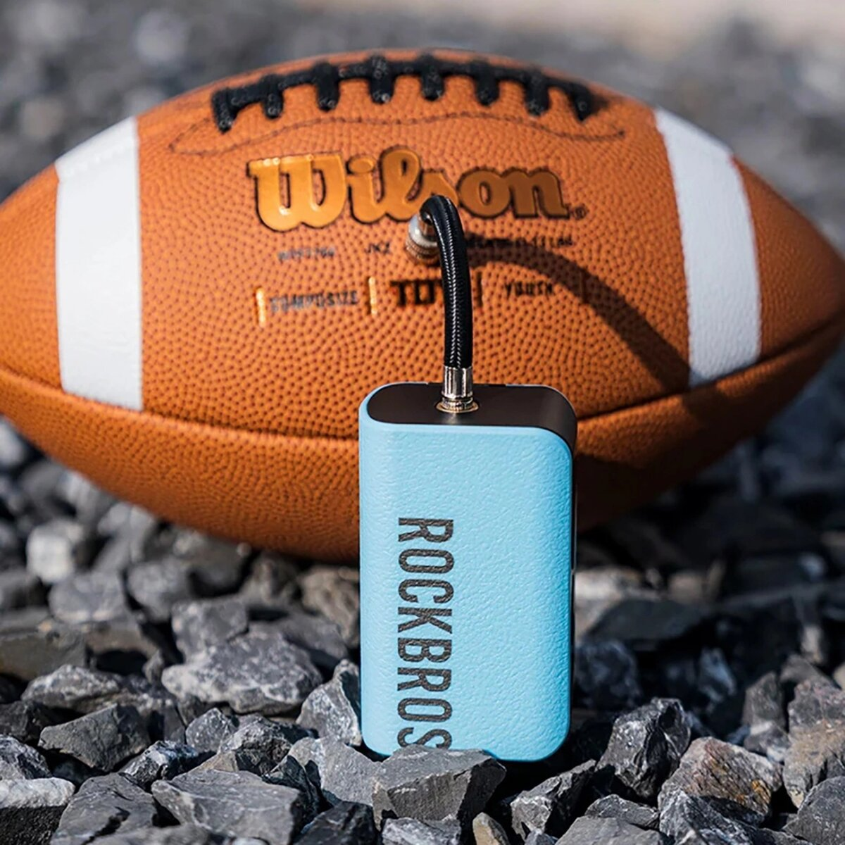 Eine blaue Rockbros Luftpumpe mit schwarzem Schlauch, ein Football und Steine.